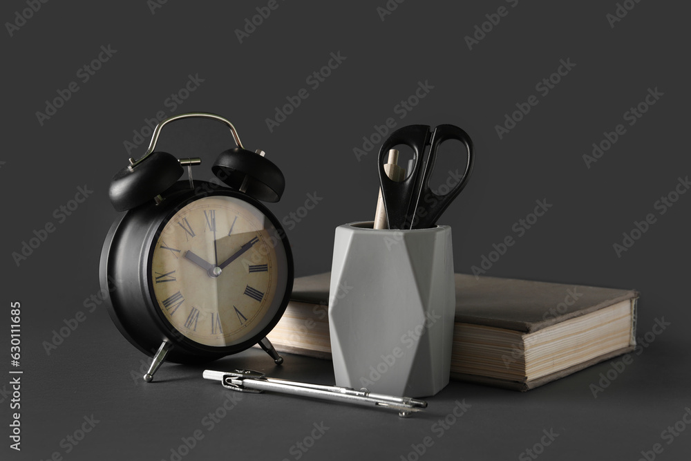 Holder with stationery, book and alarm clock on dark background