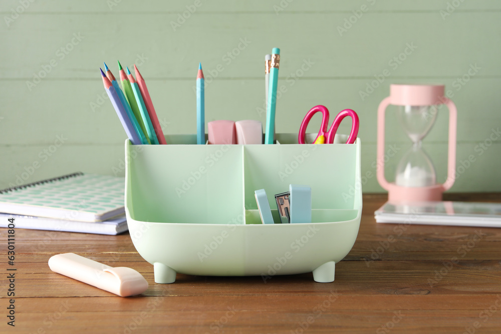 Holder with different stationery and hourglass on wooden table