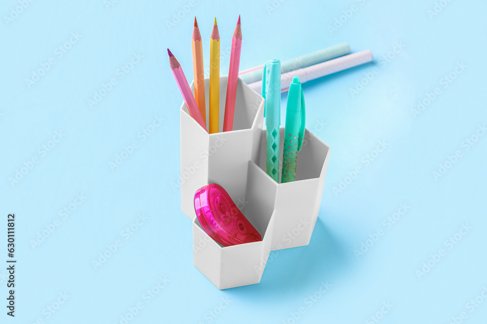 Holder with different pens, pencils and adhesive tape on color background