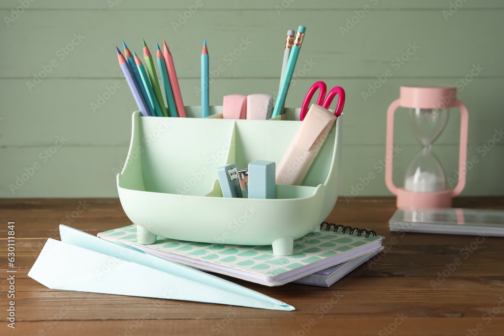 Holder with different stationery and hourglass on wooden table