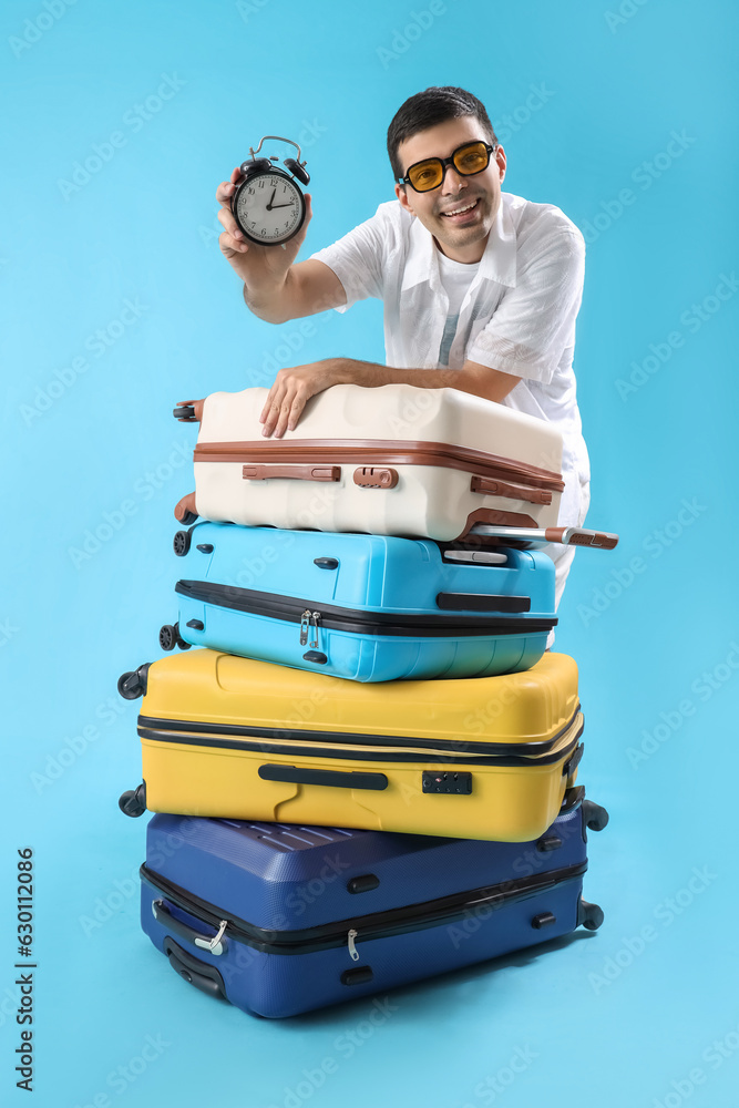 Male tourist with suitcases and clock on blue background. Time to travel