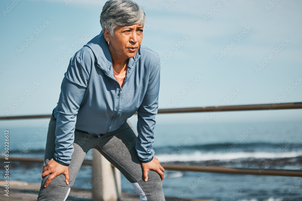 Senior, fitness and tired woman at the beach on break from training, workout or morning cardio run i