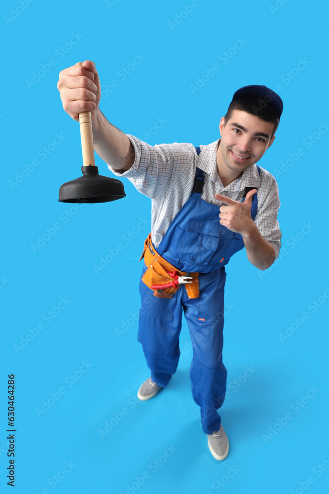 Young male plumber pointing at plunger on blue background