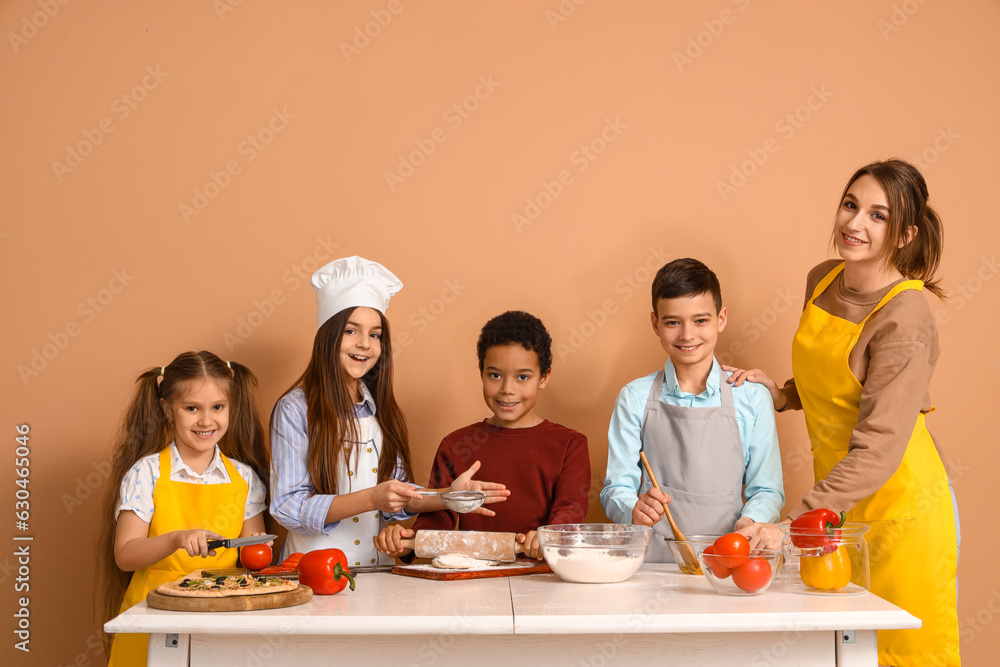 Female chef with group of little children during cooking class on beige background