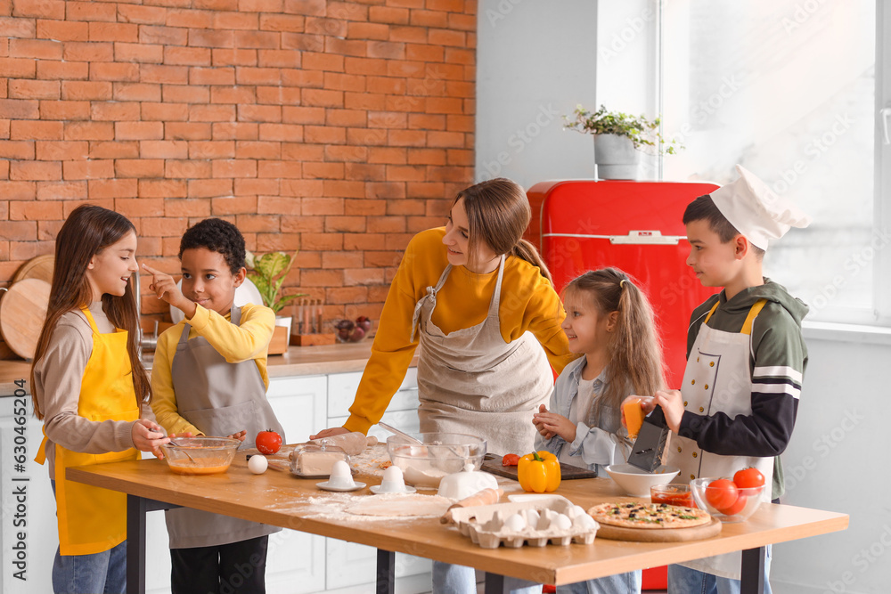 Female chef with group of little children preparing pizza during cooking class in kitchen