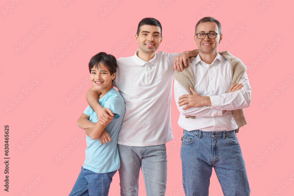 Happy little boy with his dad and grandfather on pink background