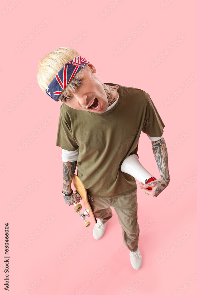 Tattooed young man with skateboard and megaphone on pink background