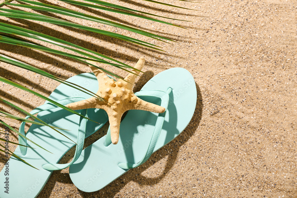 Flip-flops with starfish and palm leaf on sand