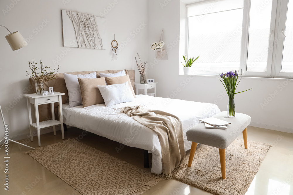 Interior of bright bedroom with beautiful iris flowers on bedside bench