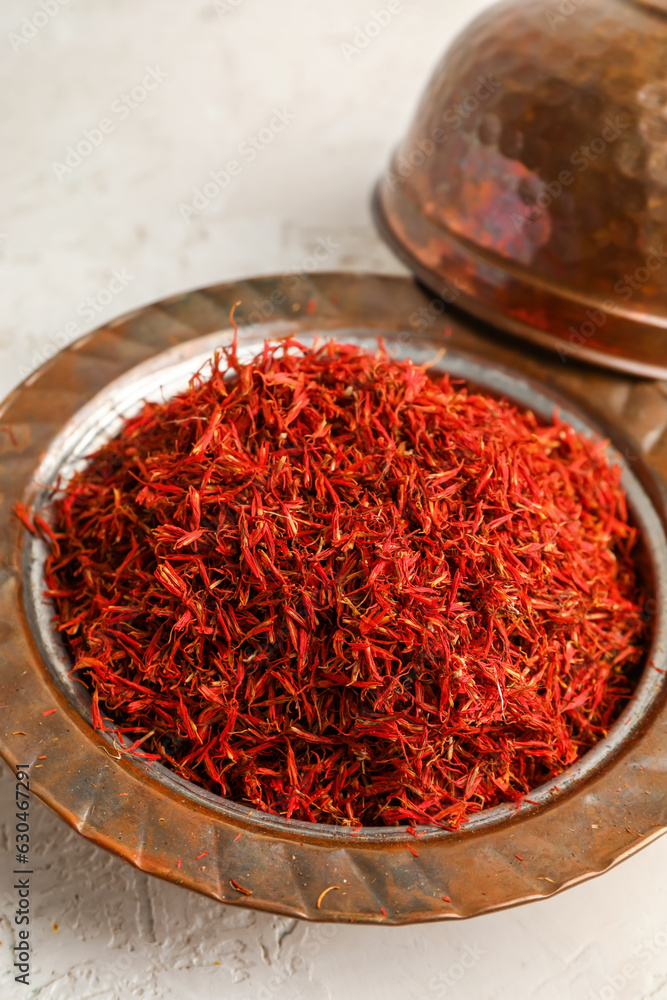 Bowl with pile of saffron on light background