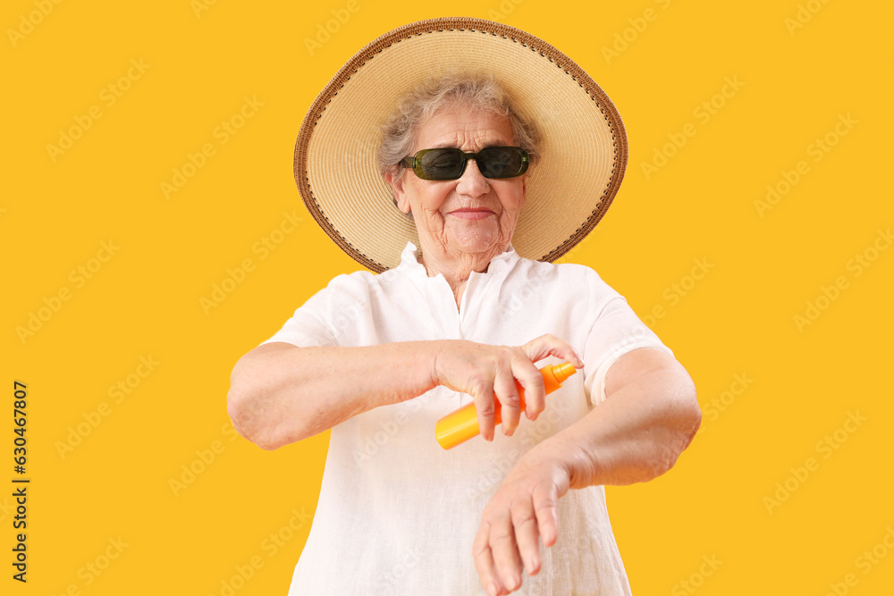 Senior woman applying sunscreen cream on orange background