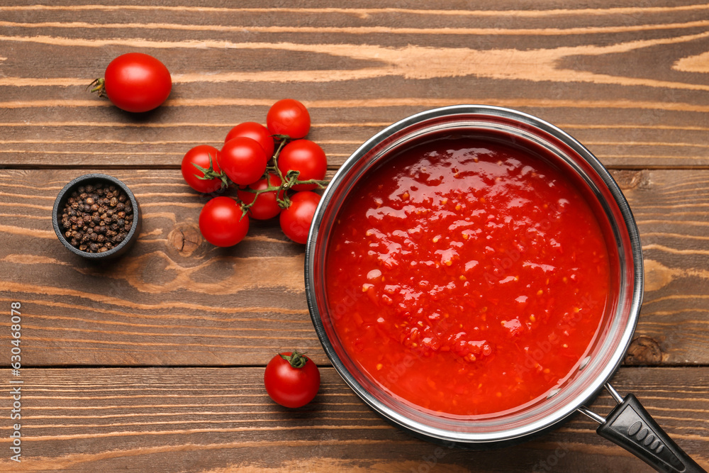 Saucepan with tasty tomato sauce and fresh vegetables on wooden background