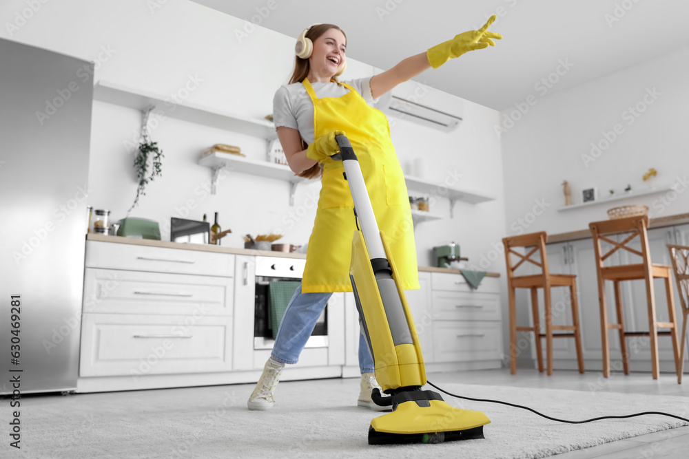 Young woman with headphones hoovering carpet in kitchen