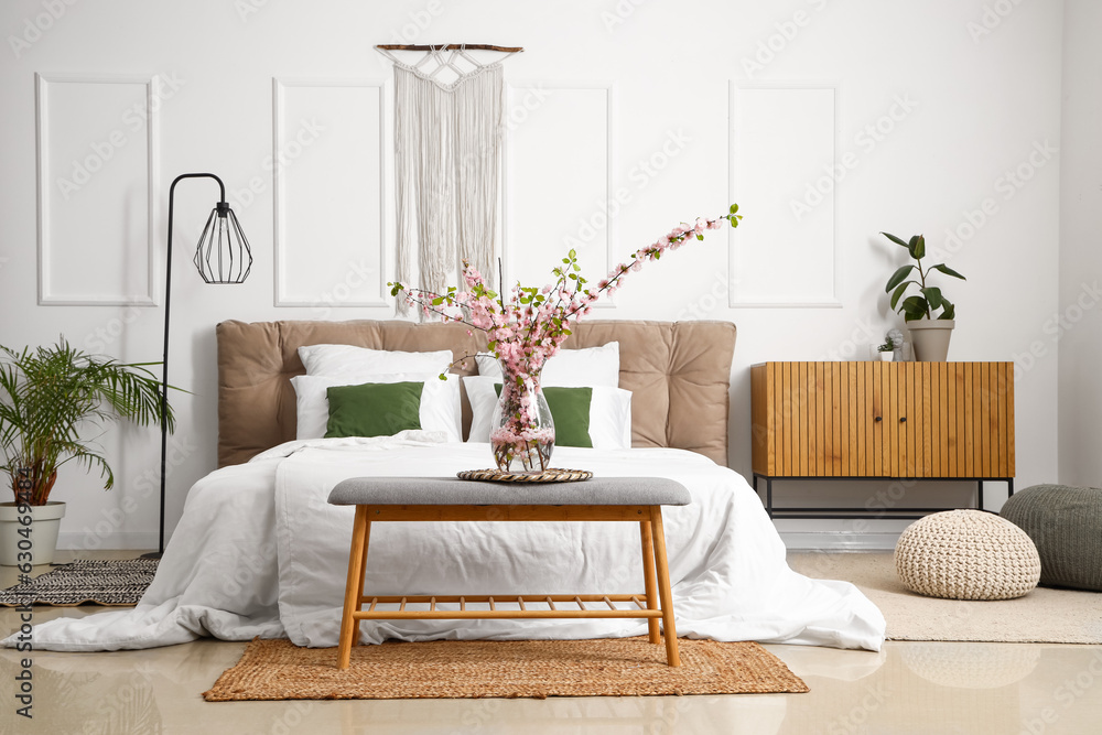 Interior of light bedroom with blooming tree branches on bedside bench