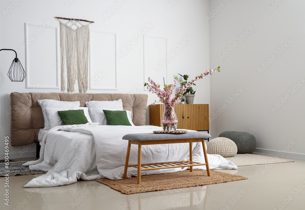 Interior of light bedroom with blooming tree branches on bedside bench