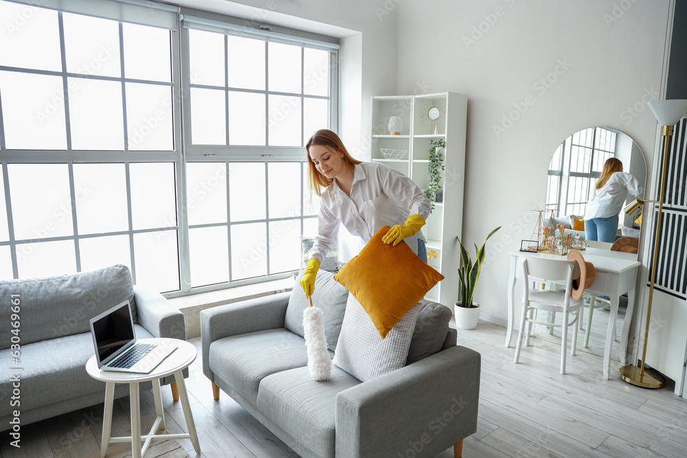 Young woman cleaning sofa with pp-duster at home