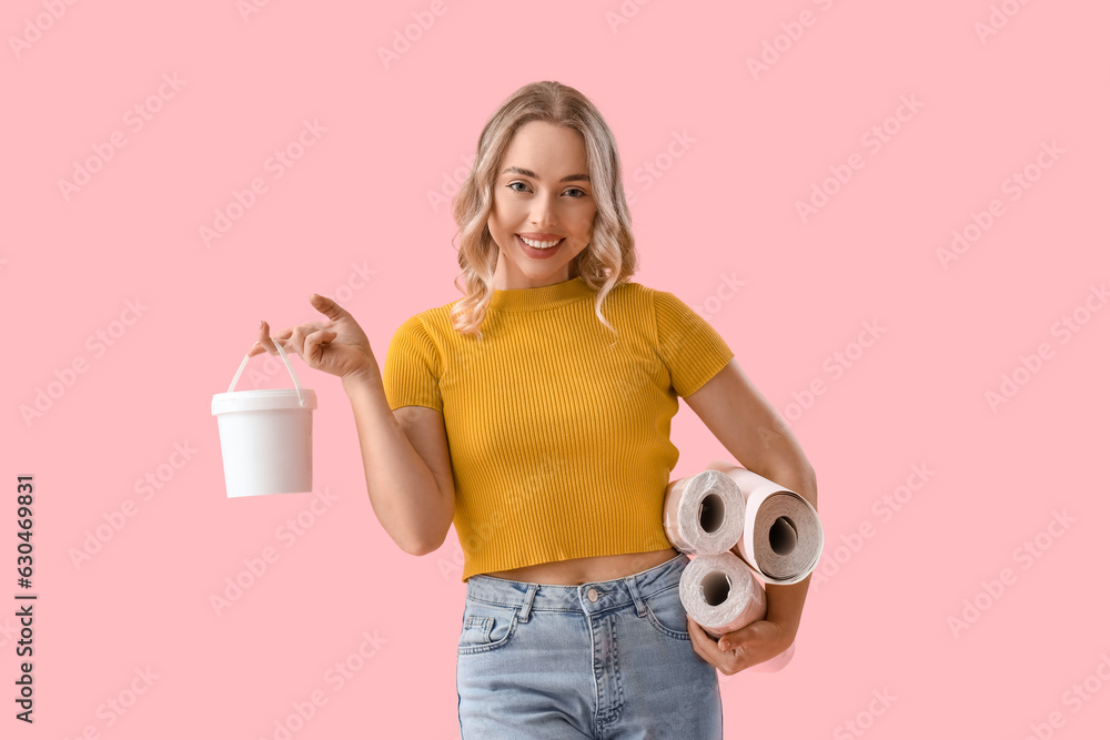 Young woman with wallpaper rolls and glue on pink background