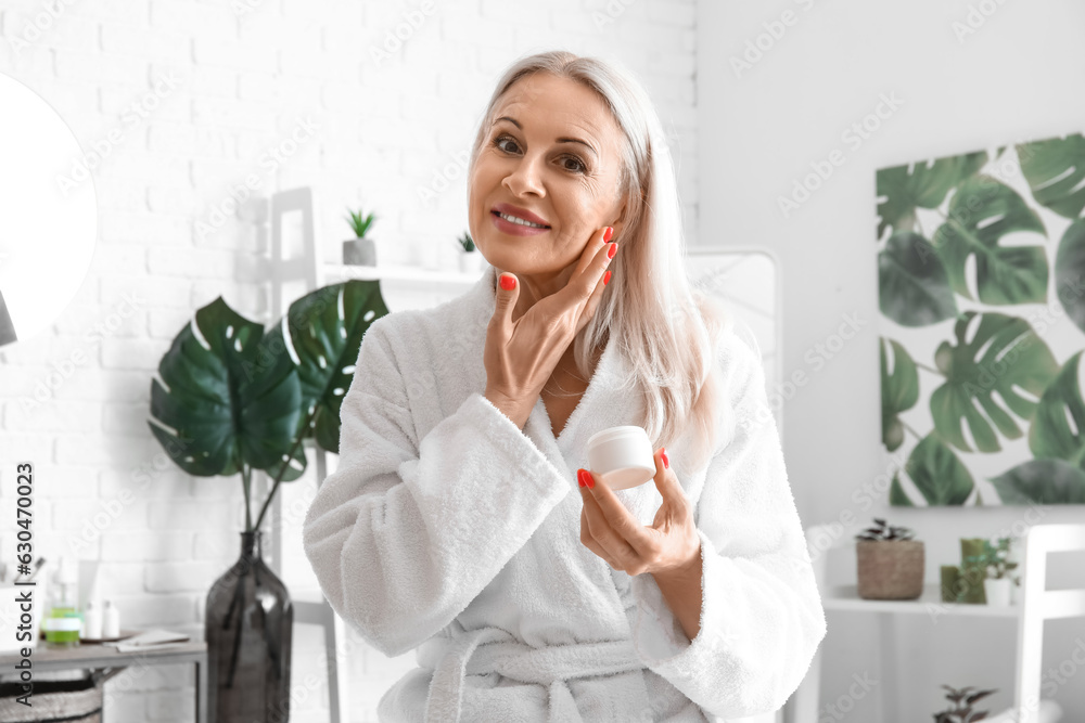 Mature woman applying facial cream in bathroom