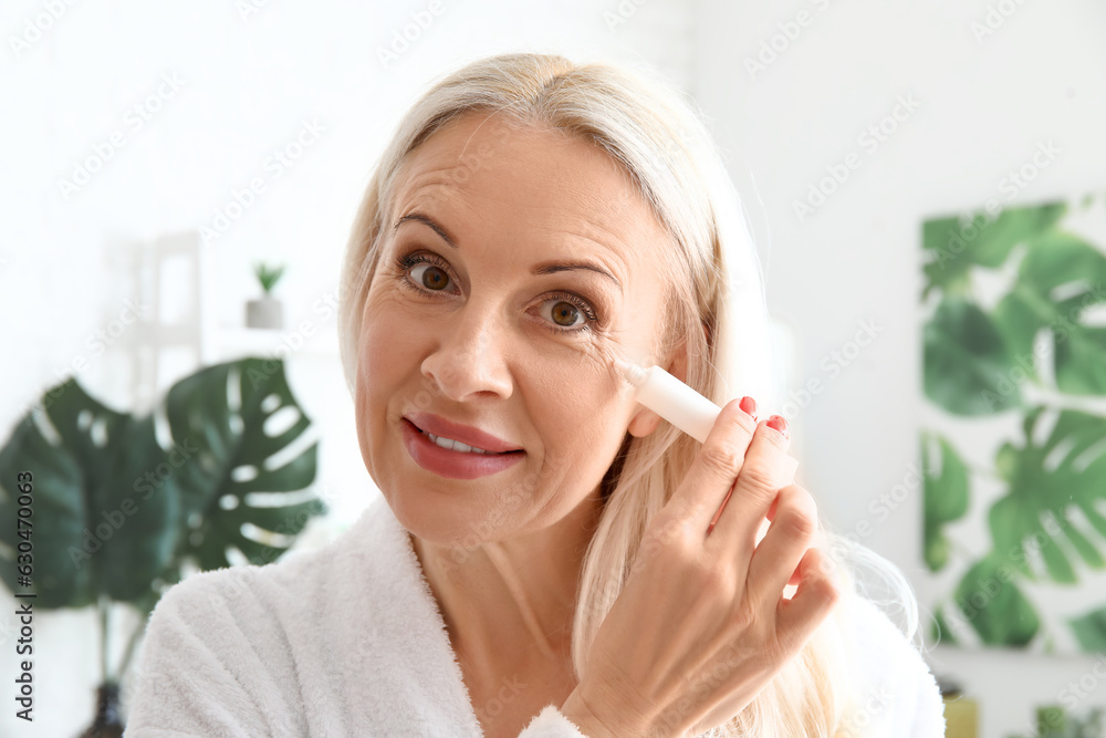 Mature woman applying under-eye cream in bathroom, closeup