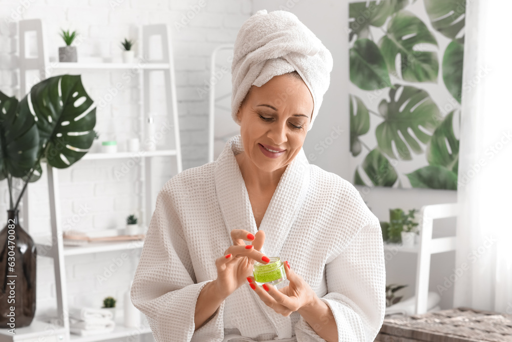 Mature woman applying facial cream in bathroom