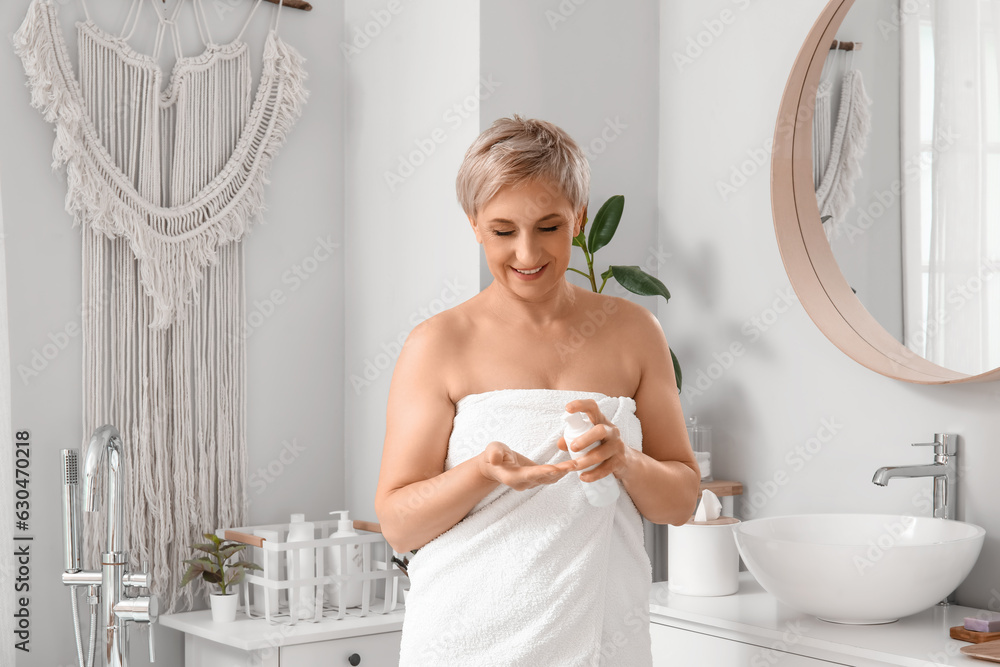 Mature woman applying cream in bathroom