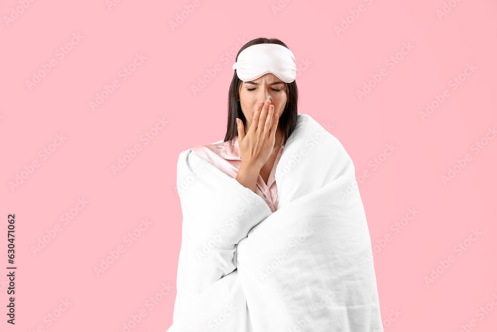 Young woman with sleeping mask and blanket on pink background