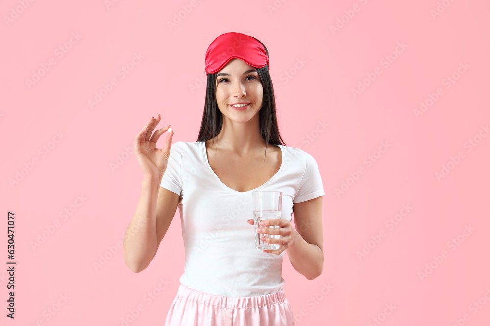 Young woman with pill and glass of water on pink background