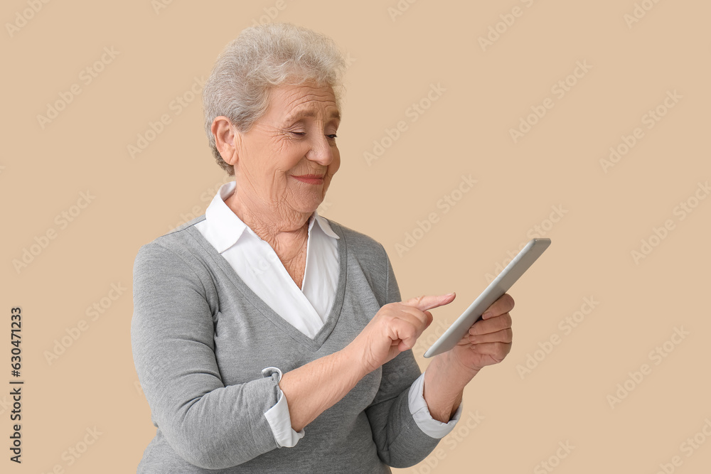 Senior woman using tablet computer on beige background