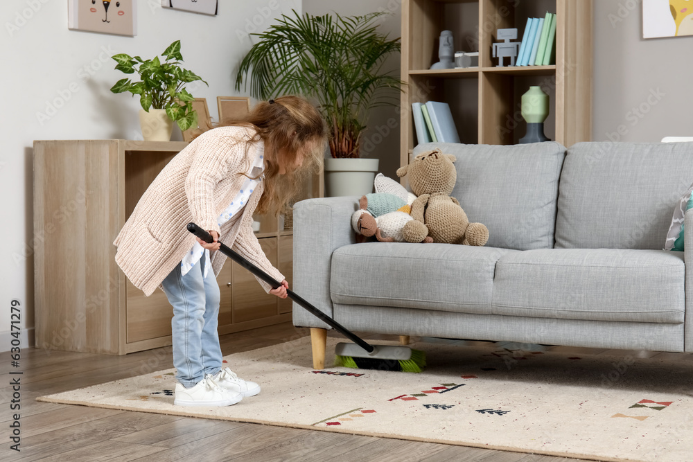 Cute little girl sweeping carpet with broom at home