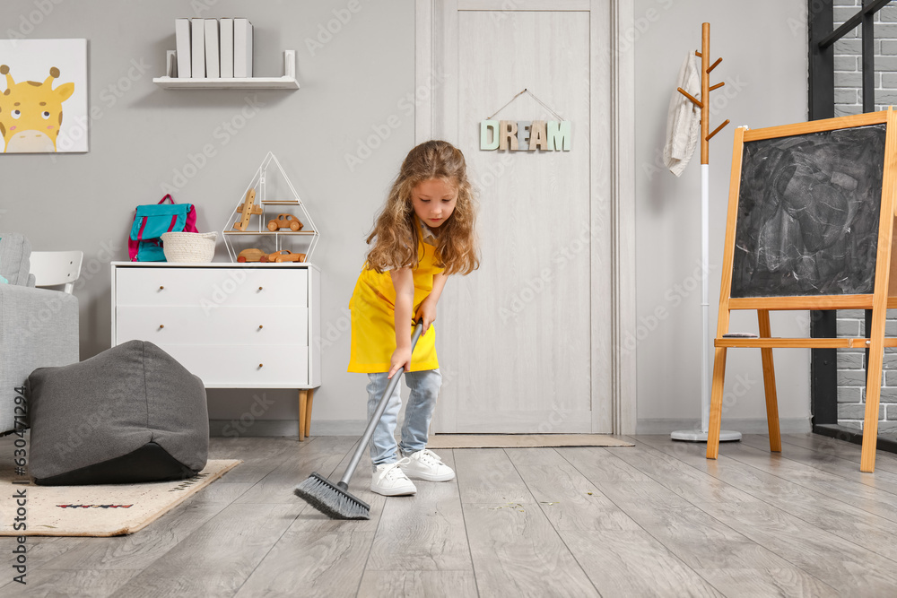 Cute little girl sweeping floor with broom at home