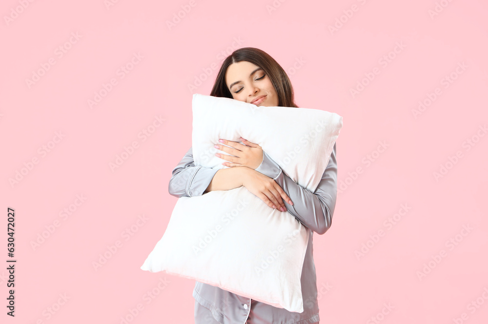 Young woman in pajamas with pillow on pink background