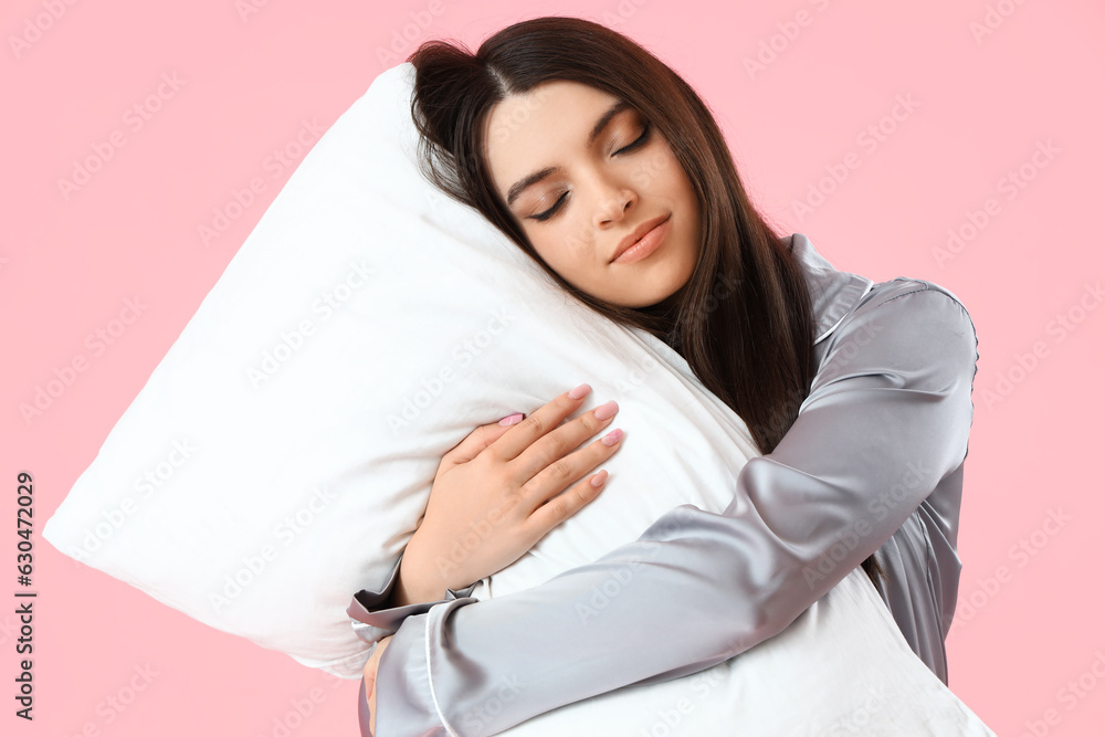 Young woman in pajamas with pillow on pink background