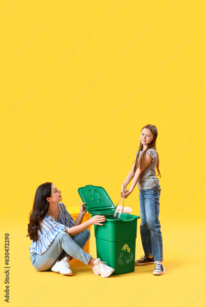 Little girl with her mother throwing glass bottle in recycle bin on yellow background