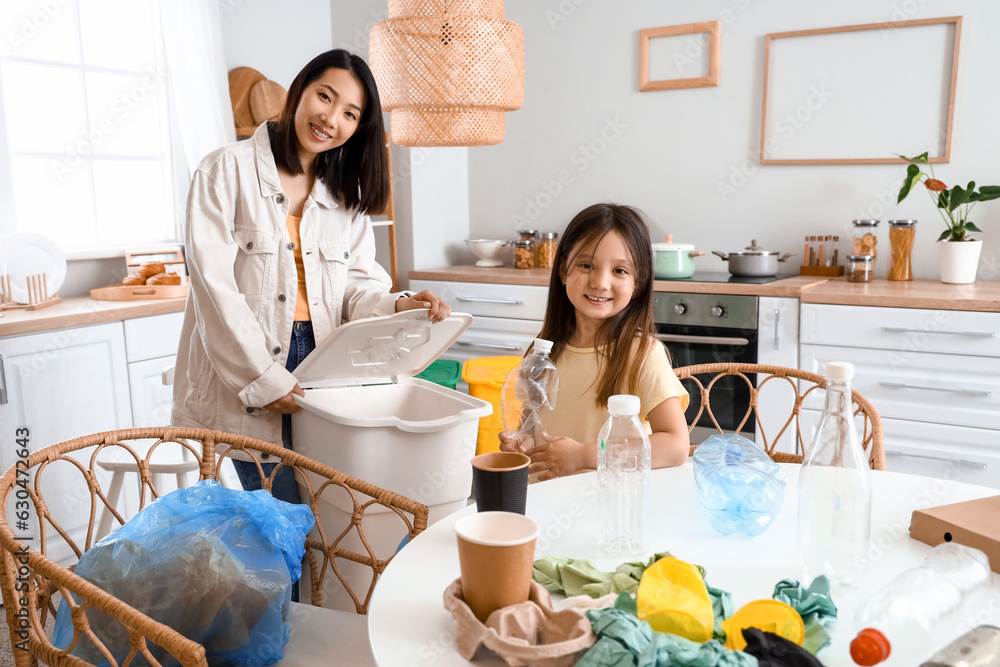 Asian mother with her little daughter sorting garbage with recycle bin in kitchen