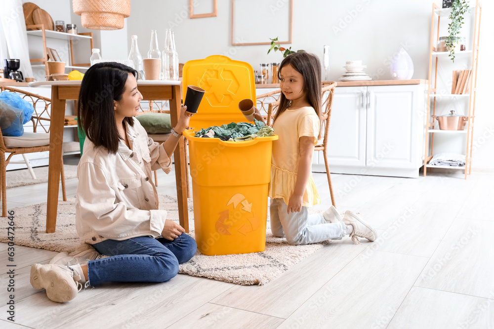 Asian mother with her little daughter throwing paper cups in recycle bin at home