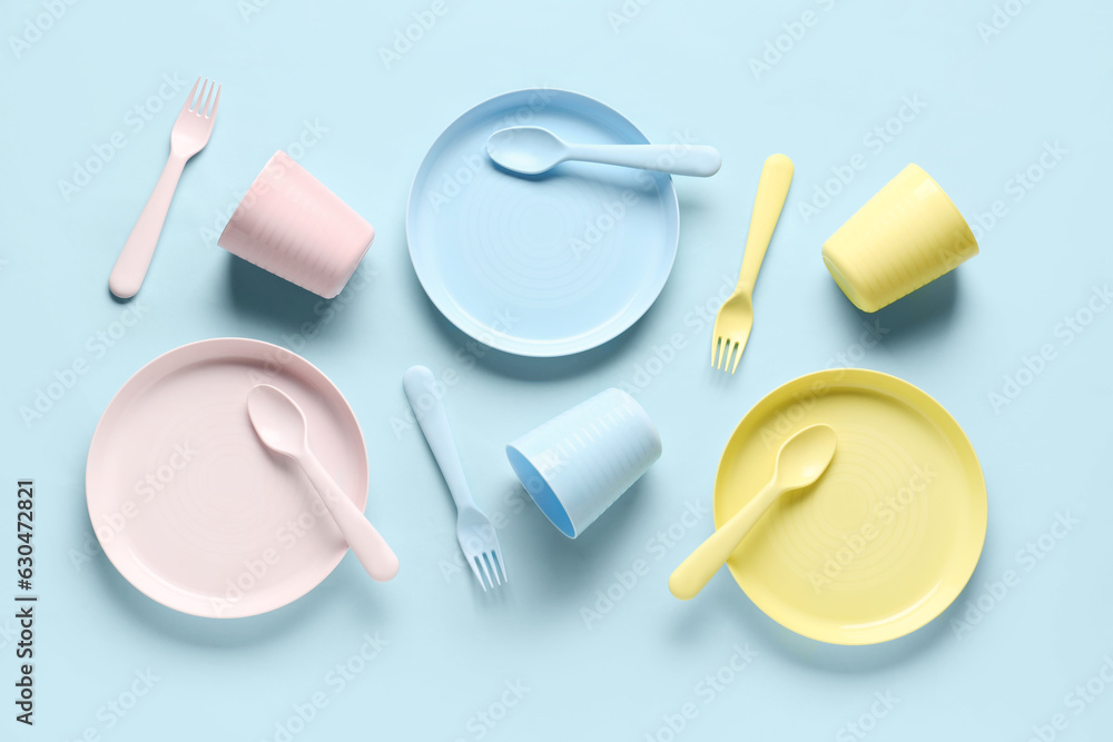 Plates with cups and cutlery for baby on blue background