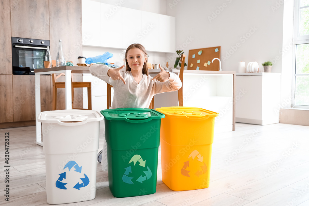 Little girl pointing at recycle trash bins in kitchen