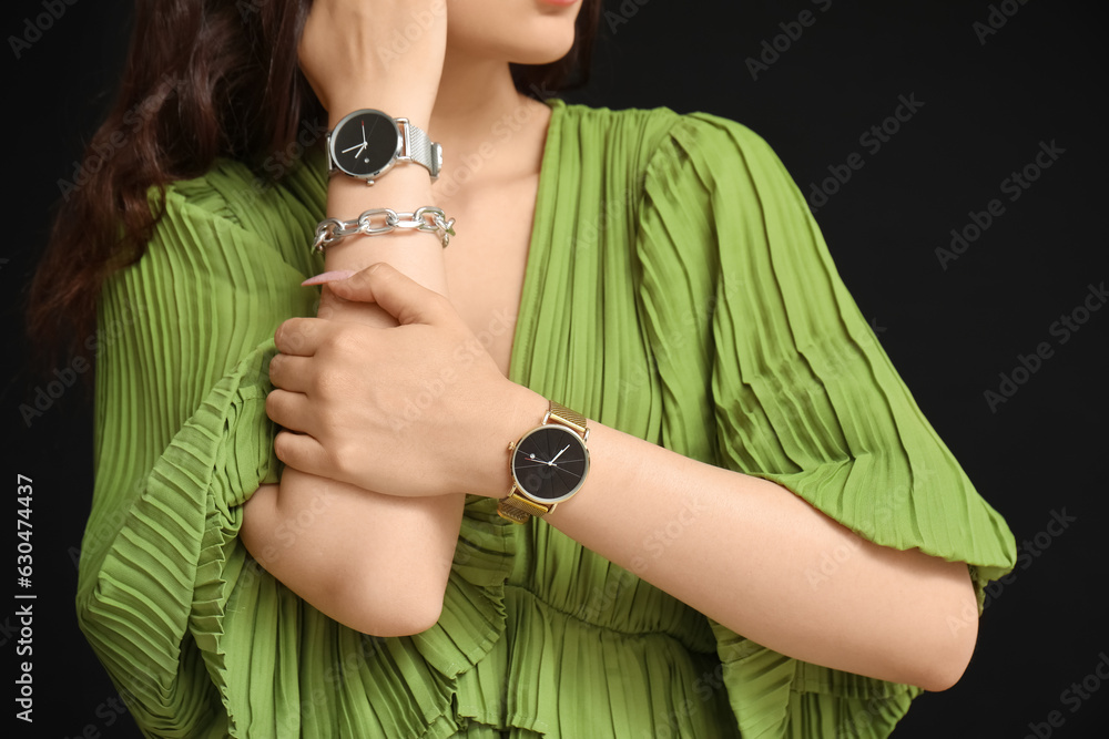 Elegant young woman with wristwatches on black background