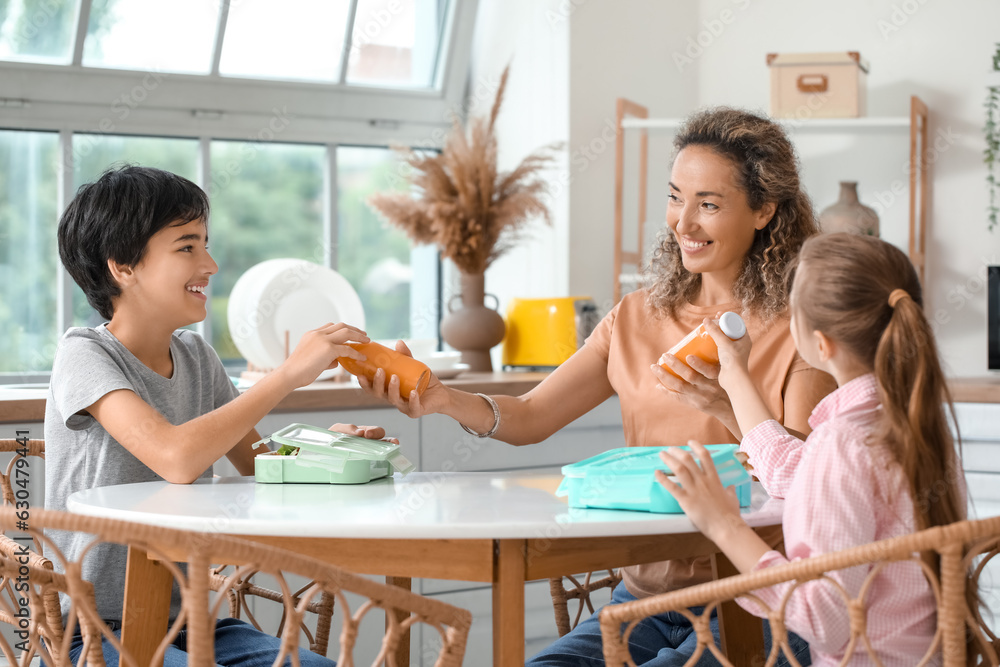 Mother giving bottles of juice to her little children in kitchen