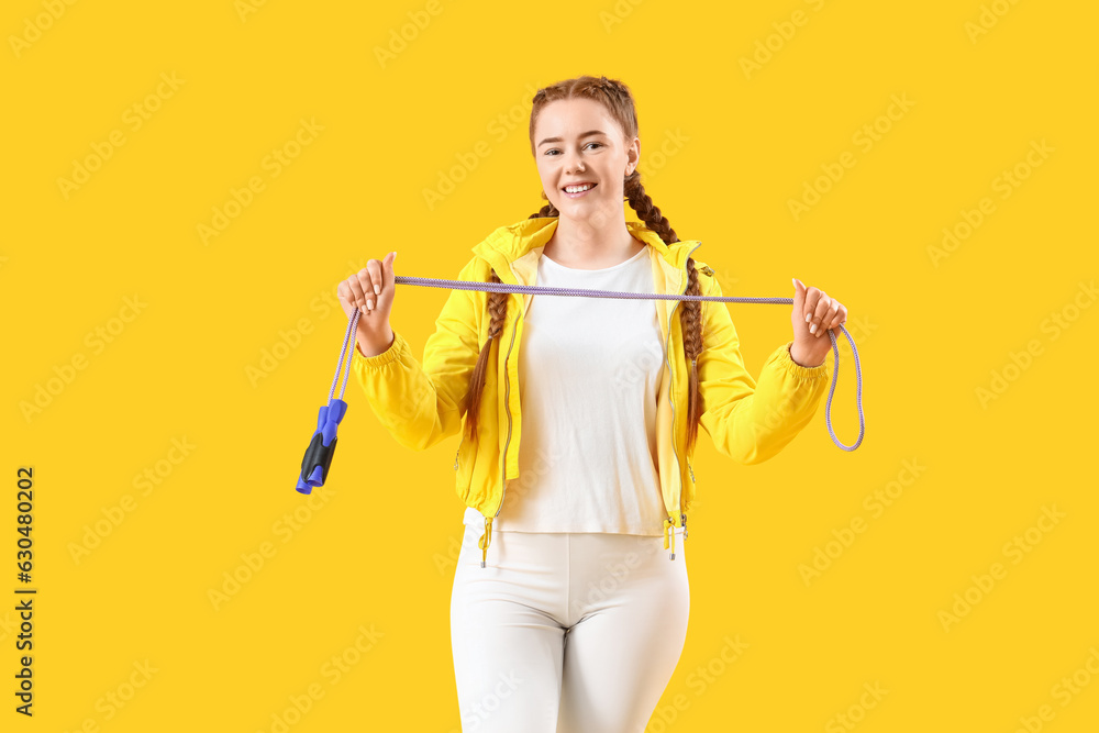 Sporty young woman with skipping rope on yellow background