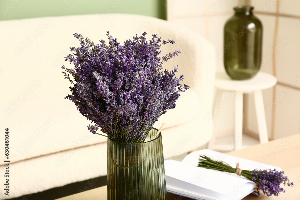 Vase with beautiful lavender flowers and book on table in interior of living room, closeup