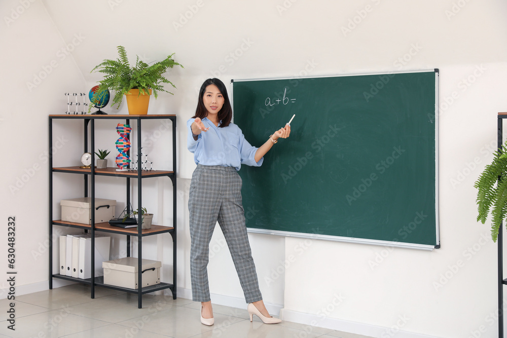 Female Asian teacher conducting Math near chalkboard in classroom