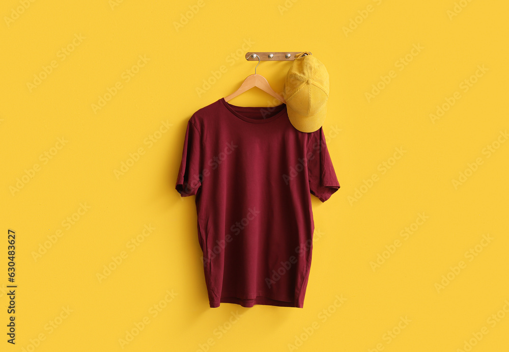 Stylish red t-shirt and cap hanging on yellow background