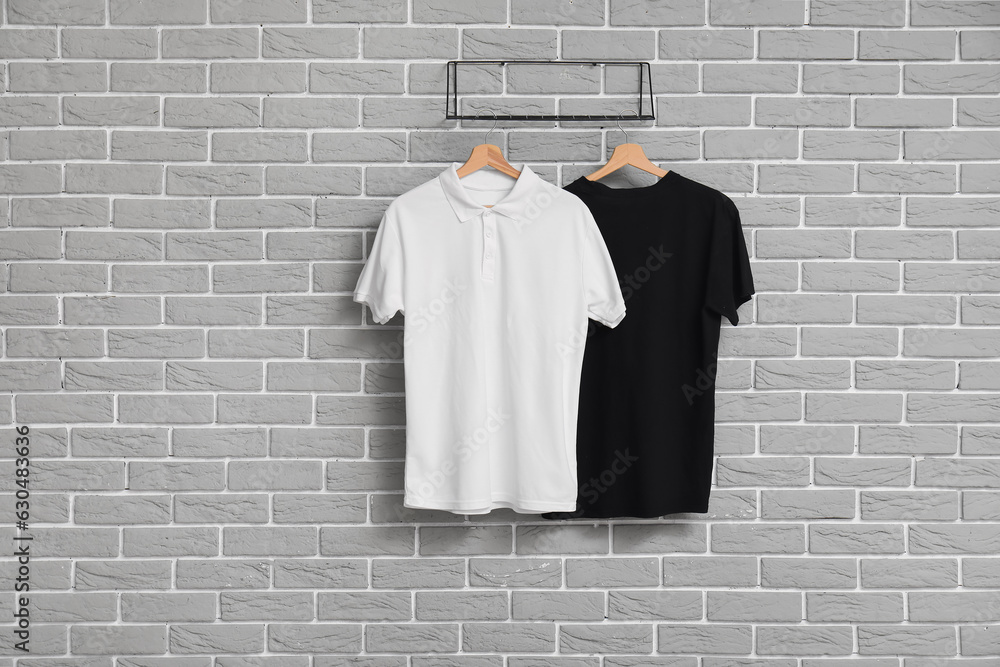 Stylish t-shirts hanging on grey brick wall