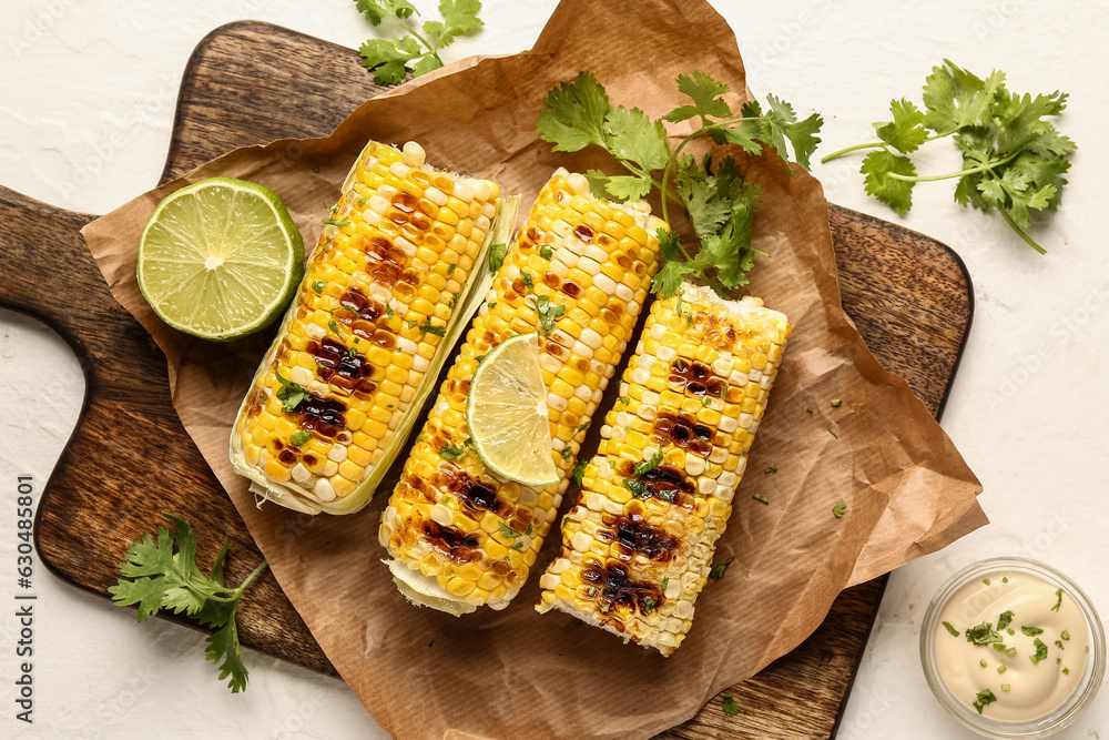 Baking paper with tasty grilled corn cobs and lime on white background