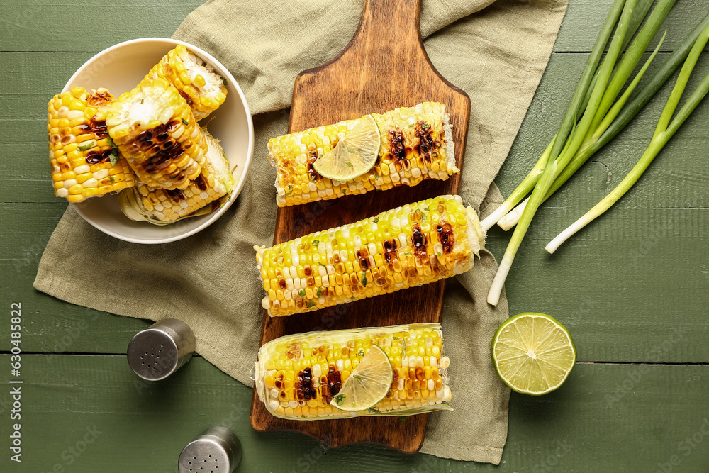 Board and bowl of tasty grilled corn cobs with lime on green wooden background