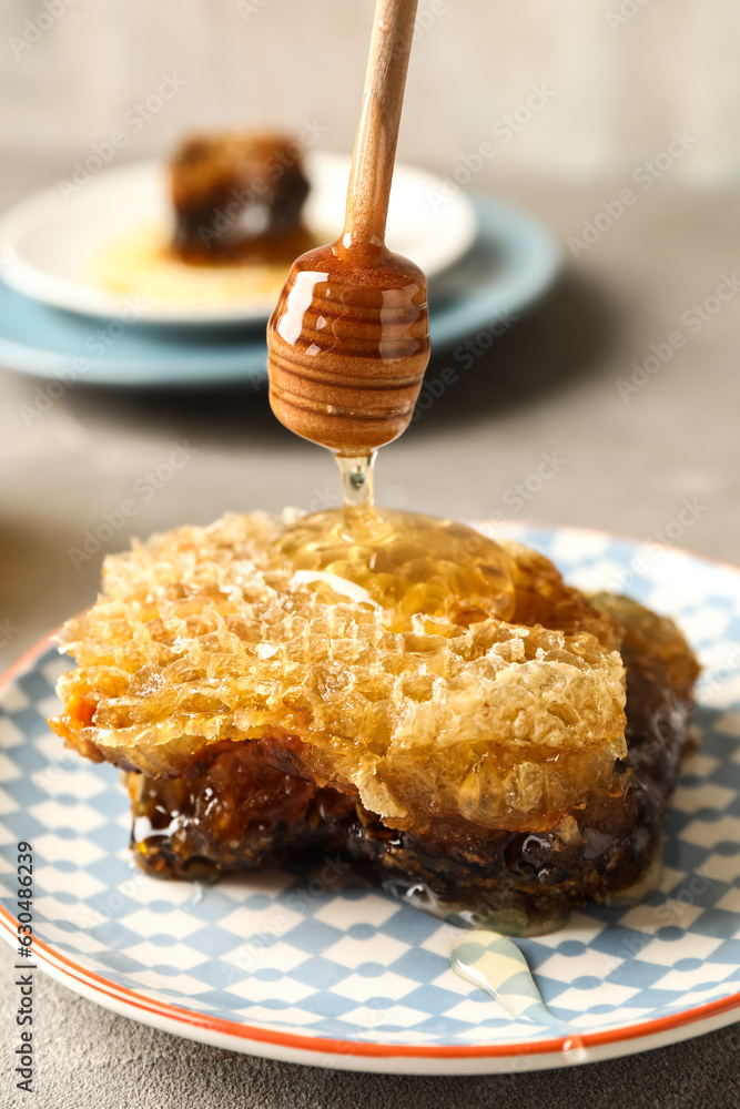 Pouring of sweet honey onto combs on grey background