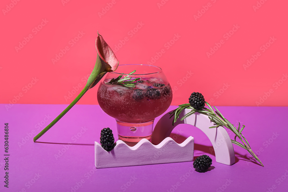 Glass of tasty blackberry cocktail with calla lily on color background