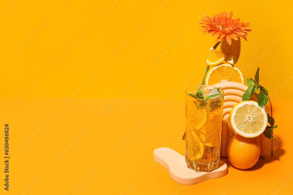 Glass of tasty citrus cocktail with fruits and flower on orange background