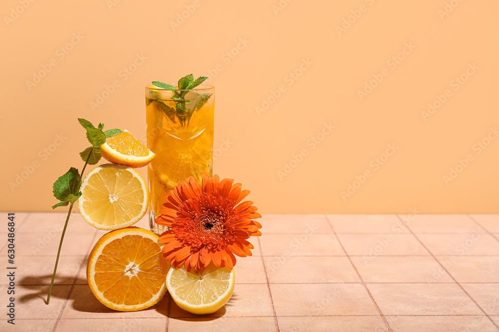 Glass of tasty citrus cocktail with fruits and flower on tile near orange wall